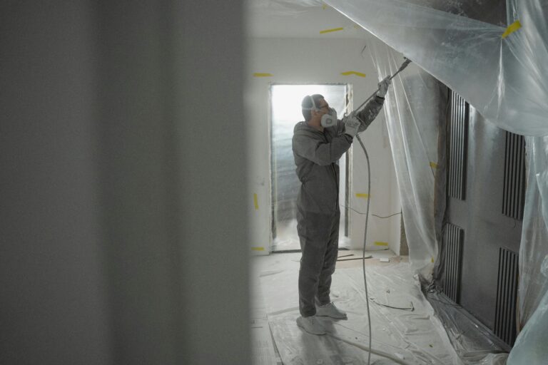 Man in protective gear spray painting a house's interior during renovation work.